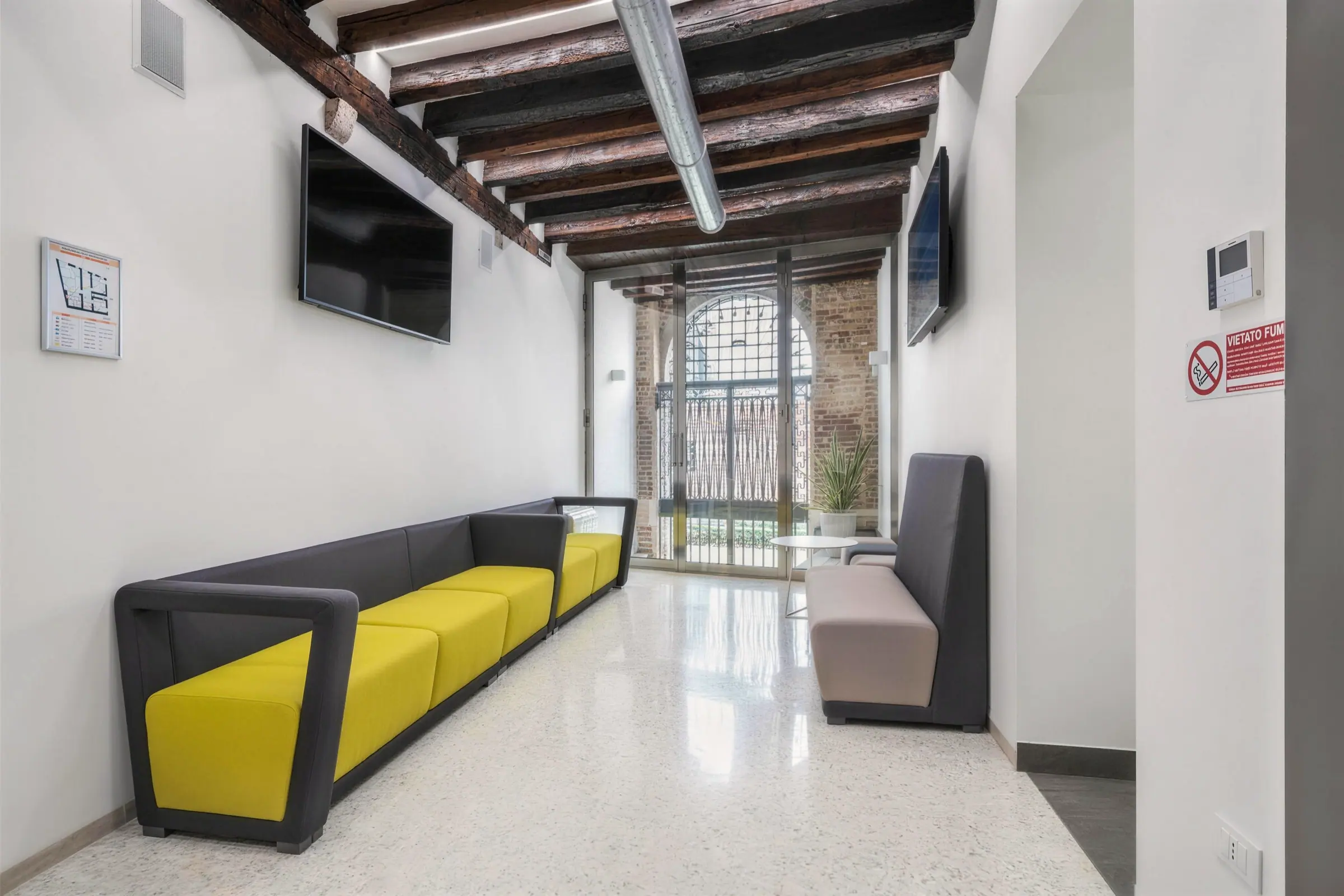 La sala d'attesa dello studio di Venezia: travi a vista, pavimento alla veneziana, divani gialli e la finestra sul rio